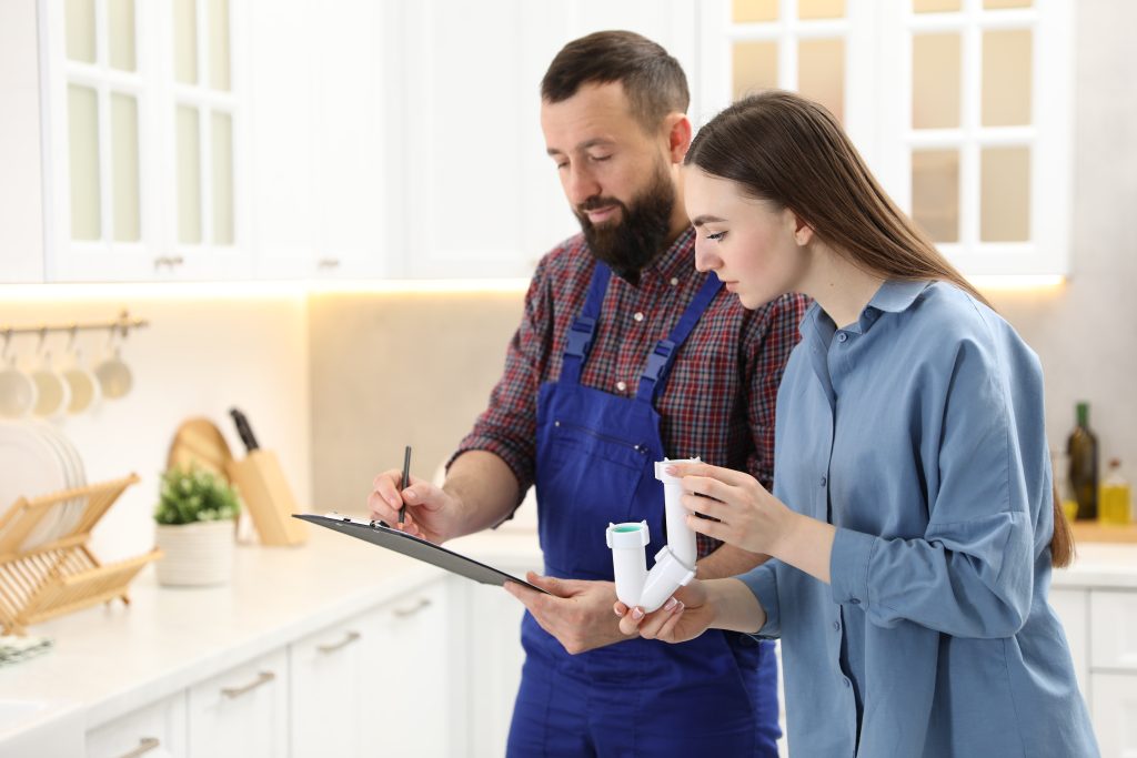 Young woman with siphon and plumber with clipboard signing documents in kitchen